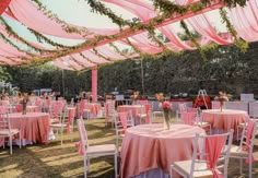 tables and chairs covered in pink cloths under an awning at a wedding reception