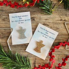 two christmas cards sitting on top of a wooden table next to red flowers and greenery