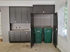 an empty garage with two trash cans in the middle and one green bin on the other side