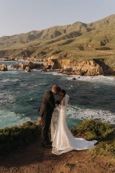 a bride and groom kissing on the cliff overlooking the ocean