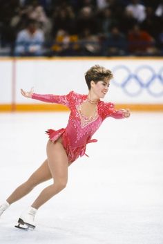 a woman skating on an ice rink wearing a pink outfit and white shoes with her arms outstretched