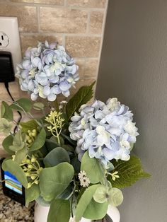 a vase filled with blue and white flowers on top of a counter next to a phone