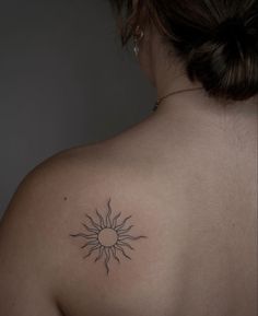 a woman's back with a tattoo on her left shoulder and the sun in the middle