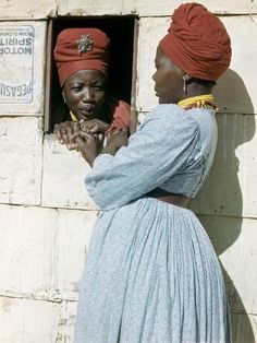 two women standing in front of a white brick wall and one is holding her hand out to the other woman