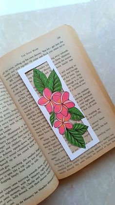 an open book with some pink flowers on the page and green leaves sticking out of it