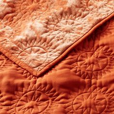 an orange quilted bed spread with white and brown designs on the edges, close up