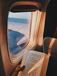 a person is reading a book while looking out an airplane window