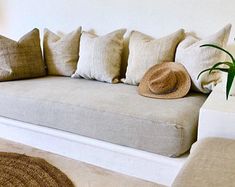 a white couch with many pillows and a hat on it's back rest area