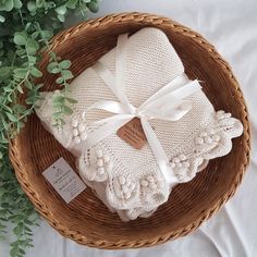 two white knitted blankets in a wicker basket next to some green plant leaves