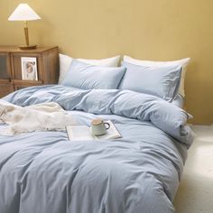 a blue comforter on a bed with pillows and a book next to it in front of a lamp