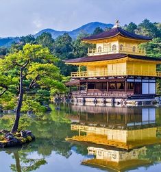 a yellow building sitting on top of a lake next to a lush green forest covered hillside