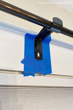 a piece of blue tape is taped to the side of a window frame with a metal bar