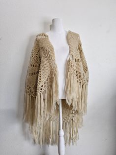 a white mannequin wearing a crocheted shawl with tassels