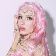 a woman with pink hair and piercings on her face posing in front of a white wall