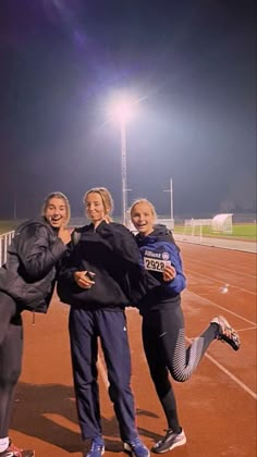 three women are posing for a photo on a track at night with their arms around each other