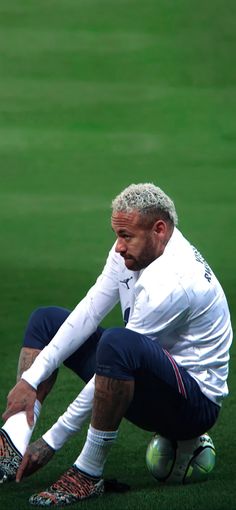 a man sitting on top of a soccer field next to a green ball in his hand