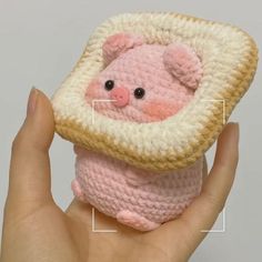 a hand holding a small crocheted pink and white pig in a square frame