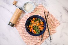 a blue bowl filled with food next to chopsticks and a salt shaker