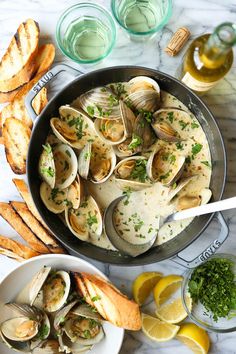 clams and bread in a skillet on a marble table with lemon wedges