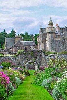 an old castle with lots of flowers in the foreground and a path leading to it