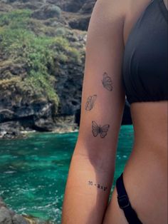 a woman with a butterfly tattoo on her arm next to the ocean and rocks in the water