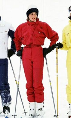 three skiers standing in the snow with their ski gear on and one is wearing a red suit