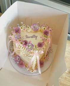 a heart shaped cake in a white box with pink and purple flowers on the side