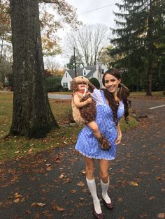 a woman in a blue dress holding a teddy bear while standing next to a tree