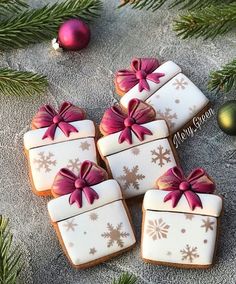 four decorated cookies with bows and snowflakes on them next to christmas tree branches