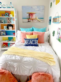 a white bed topped with lots of pillows next to a book shelf filled with books