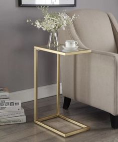 a gold side table with flowers on it in front of a beige chair and gray wall