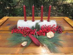 a wooden table topped with candles and pine cones covered in frosting next to red berries