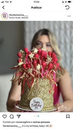 a woman holding a birthday cake decorated with red and gold sprinkles