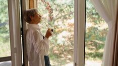 a woman standing in front of a glass door holding a drink and looking out the window