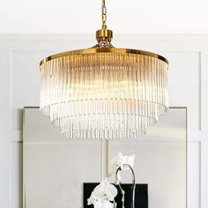 a chandelier hanging over a dining room table with flowers on it and a mirror in the background