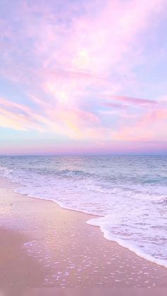 two people walking on the beach with surfboards under a pink and blue cloudy sky