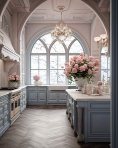 a large kitchen with blue cabinets and pink flowers in vases on the counter top