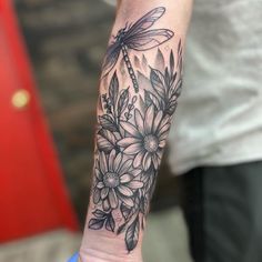 a woman's arm with flowers and dragonfly tattoo on her left forearm, while the rest of the arm is black and white