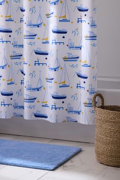 a bath room with a blue rug and a shower curtain that has boats on it