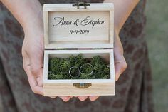 two wedding rings in a wooden box with moss on the inside, and their date