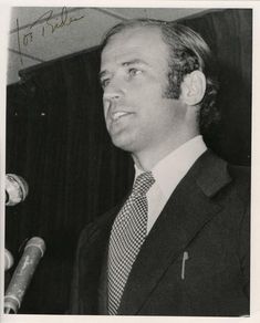 a black and white photo of a man in a suit standing next to a microphone