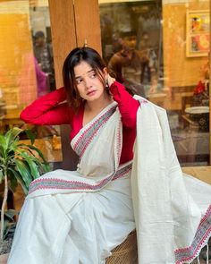 a woman sitting on top of a chair wearing a white sari and red shirt