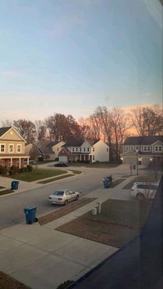 an empty street with cars parked on the side and houses in the backround