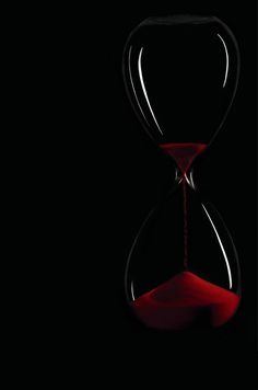 an hourglass with red sand running through it on a black background in the dark