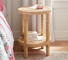 a wicker side table with books on it in front of a white curtained window