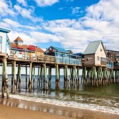 a wooden pier with houses on it next to the ocean and blue sky in the background