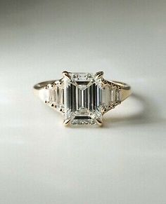 an emerald cut diamond ring on a white surface