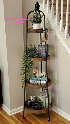 a three tiered shelf with books and plants on it in front of a stair case