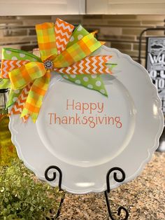 a white plate with a green and orange bow on it that says happy thanksgiving sitting on a stand