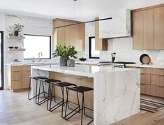 a kitchen with marble counter tops and stools in front of the island, surrounded by wooden cabinets